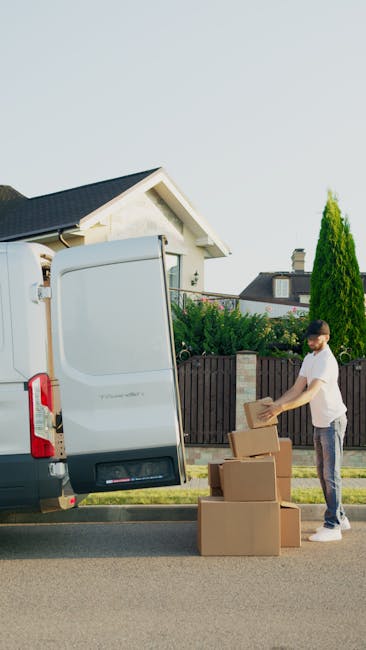 A street scene in Coulsdon featuring several parked cars along the kerbside and a moving van parked nearby on the pavement. In the foreground, cardboard boxes, foam padding, and plastic wrap are visib